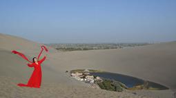 Seorang wanita berfoto bersama Air Mancur Bulan Sabit (kanan) di kawasan wisata Gunung Mingsha dan Air Mancur Bulan Sabit di Dunhuang, Jiuquan, Provinsi Gansu, Tiongkok Barat Laut, pada 19 Oktober 2025. (Adek BERRY/AFP)