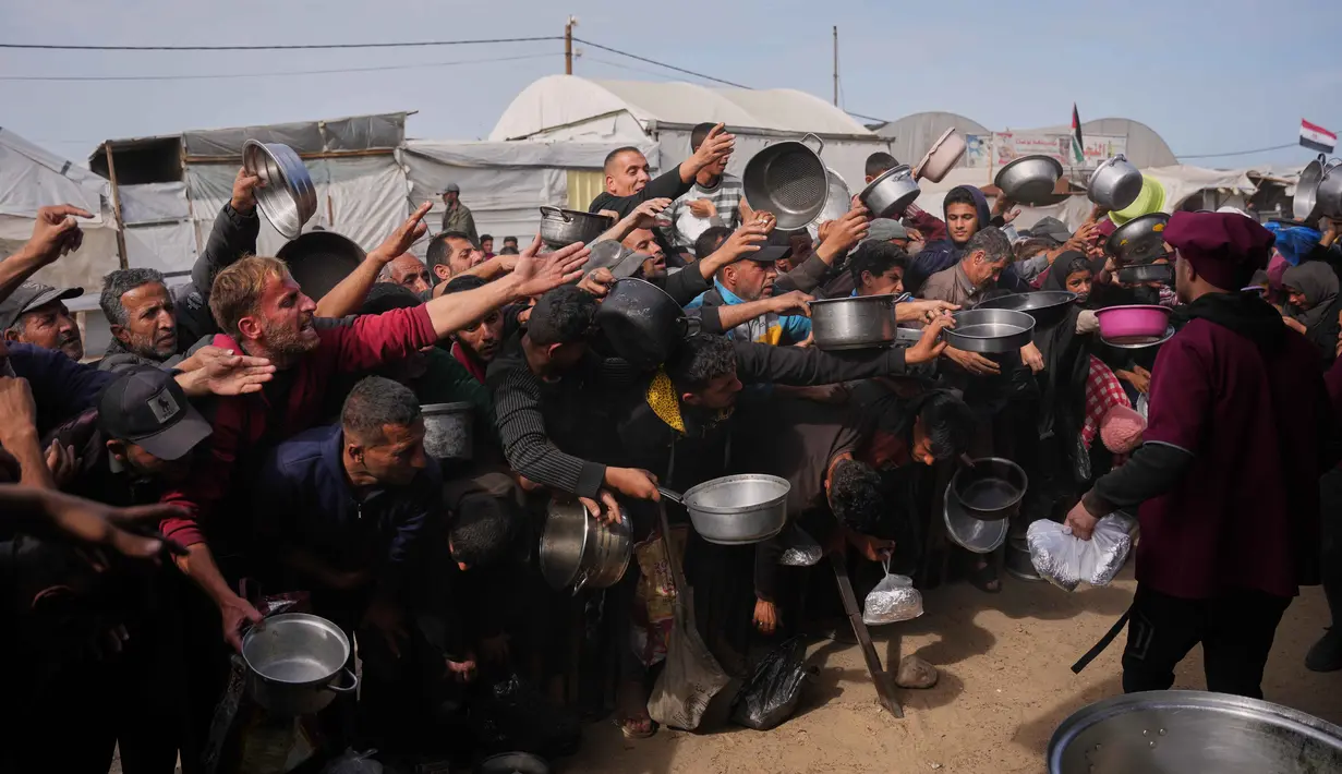 Banyak warga, termasuk anak-anak, berkumpul dengan membawa panci kosong demi mendapatkan satu porsi makanan yang disalurkan di sebuah dapur umum, Khan Younis, Jalur Gaza selatan. Tampak dalam foto, warga Palestina berebut menerima makanan sumbangan di dapur umum, Khan Younis, Jalur Gaza selatan, Jumat 6 Februari 2026. (AP Photo/Abdel Kareem Hana)