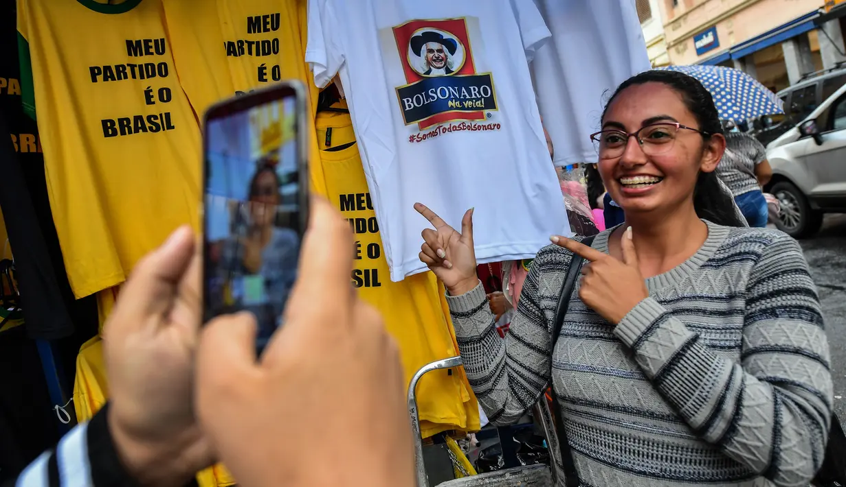 Seorang wanita berfoto dengan kaus bergambar Capres Brasil, Jair Bolsonaro dari sayap kanan di sebuah toko pinggir jalan yang populer di Sao Paulo, 8 Oktober 2018. Bolsonaro unggul dalam penghitungan suara pemilu putaran pertama. (AFP/NELSON ALMEIDA)