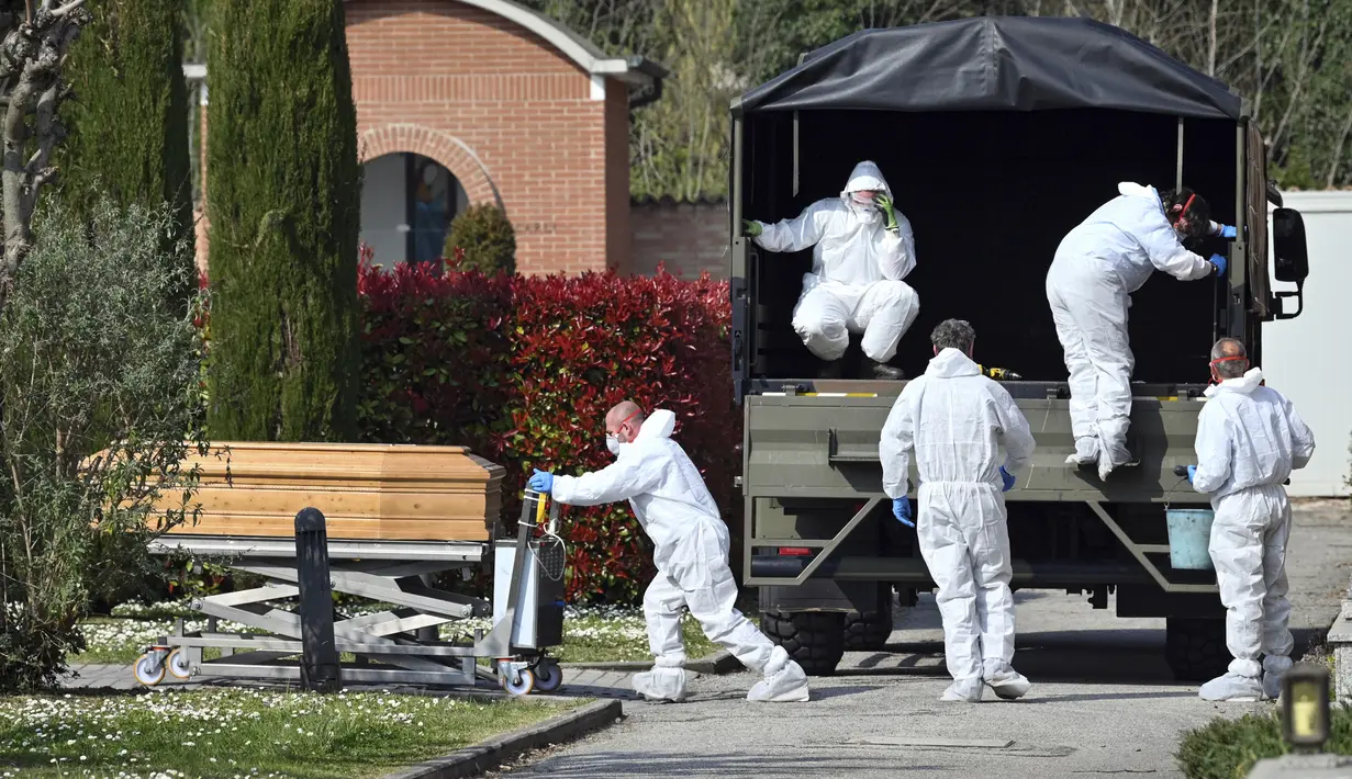 Petugas membawa peti mati berisi jasad korban virus corona COVID-19 yang diturunkan dari truk militer di pemakaman Ferrara, Italia, Sabtu (21/3/2020). Italia menghadapi krisis paling parah sejak Perang Dunia II.  (Massimo Paolone/LaPresse via AP)