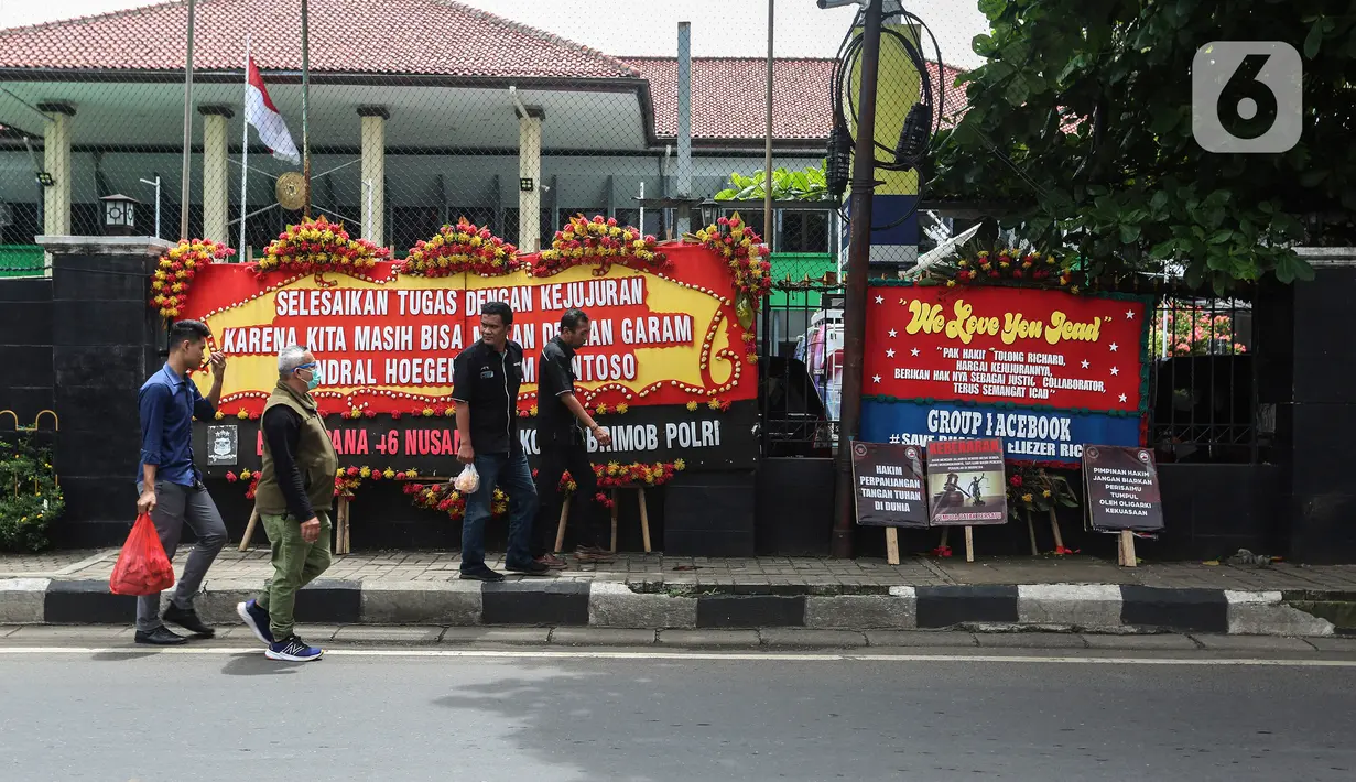 Warga melintas di depan karangan bunga saat sidang pembacaan vonis Ferdy Sambo dan Putri Candrawathi dalam kasus pembunuhan Brigadir Nofriansyah Yoshua Hutabarat di depan Pengadilan Negeri Jakarta Selatan, Senin (13/2/2023). Majelis hakim dijadwalkan membacakan vonis terdakwa Ferdy Sambo dan Putri Candrawathi. Sebelumnya Sambo dituntut hukuman penjara seumur hidup, sementara Putri penjara delapan tahun. (Liputan6.com/Johan Tallo)