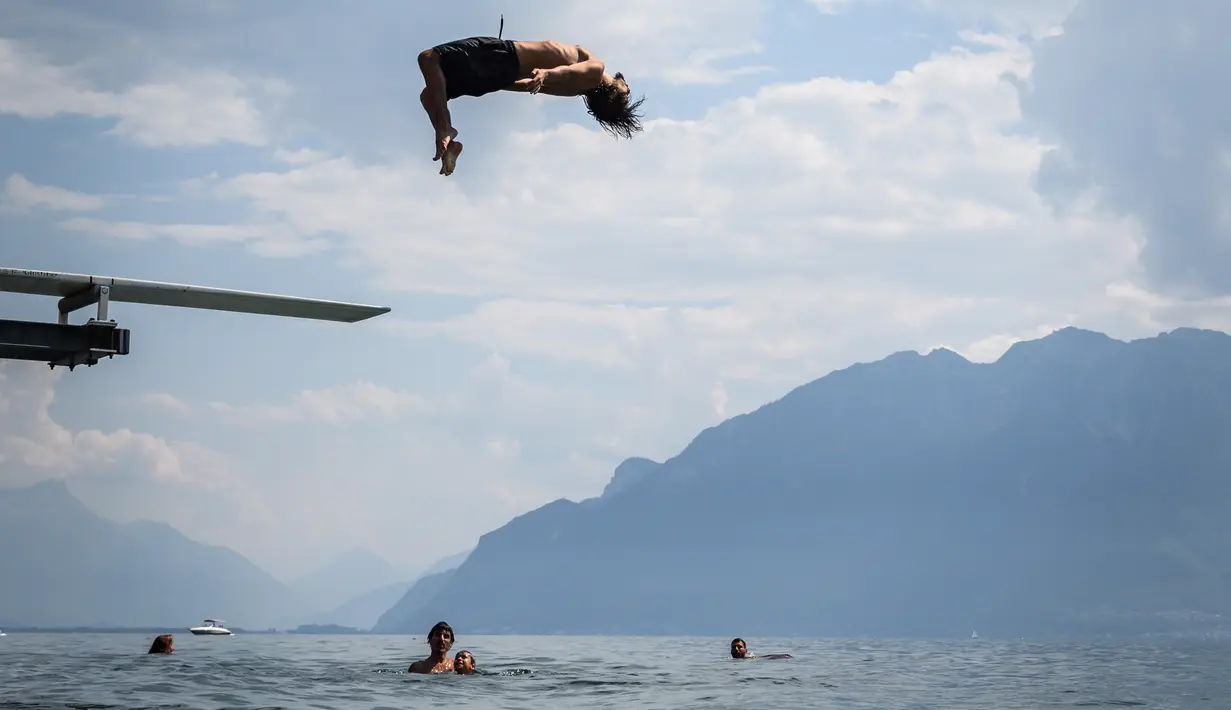 Seorang pria melompat ke Danau Jenewa di Saint Saphorin, Swiss barat saat gelombang panas melanda seluruh Eropa utara (31/7). Layanan meteorologi telah mengeluarkan peringatan gelombang panas sebagai yang terparah tahun ini. (AFP Photo/Fabrice Coffrini)