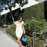 Dalam foto ini Beby Tsabina tampil kenakan dress putih yang kasual. Berpose membelakangi laut, Beby Tsabina menyempurnakan gayanya dengan menenteng tas Prada, menata rambutnya dengan gaya high-bun, dan mengenakan sneakers putih. Foto: Instagram.