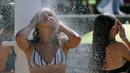 Dua wanita mendinginkan diri di bawah pancuran di pantai Biarritz, barat daya Prancis, (3/8). Cuaca panas diperkirakan akan berlangsung selama beberapa hari di eropa. (AP Photo/Bob Edme)