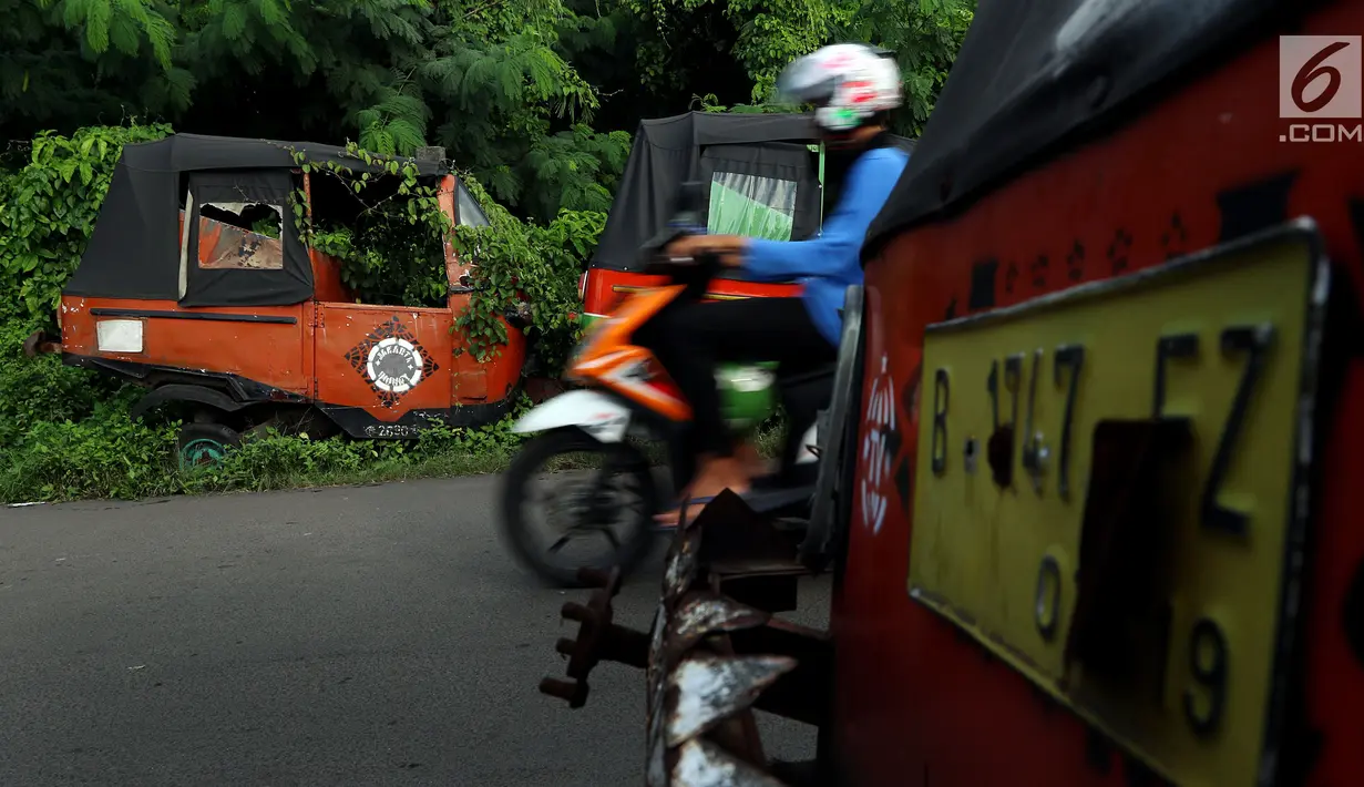 Bangkai bajaj oranye yang sudah tidak dapat digunakan diselimuti tumbuhan liar di kawasan Roxy, Jakarta Barat, Selasa (27/2). (Liputan6.com/JohanTallo)