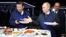 Presiden Rusia Vladimir Putin (kanan) mempersilakan Presiden China Xi Jinping (kiri) menyantap makanan saat membuat pancake bersama di sela Eastern Economic Forum di Vladivostok, Rusia, Selasa (11/9). (Sergei Bobylev/TASS News Agency Pool Photo via AP)