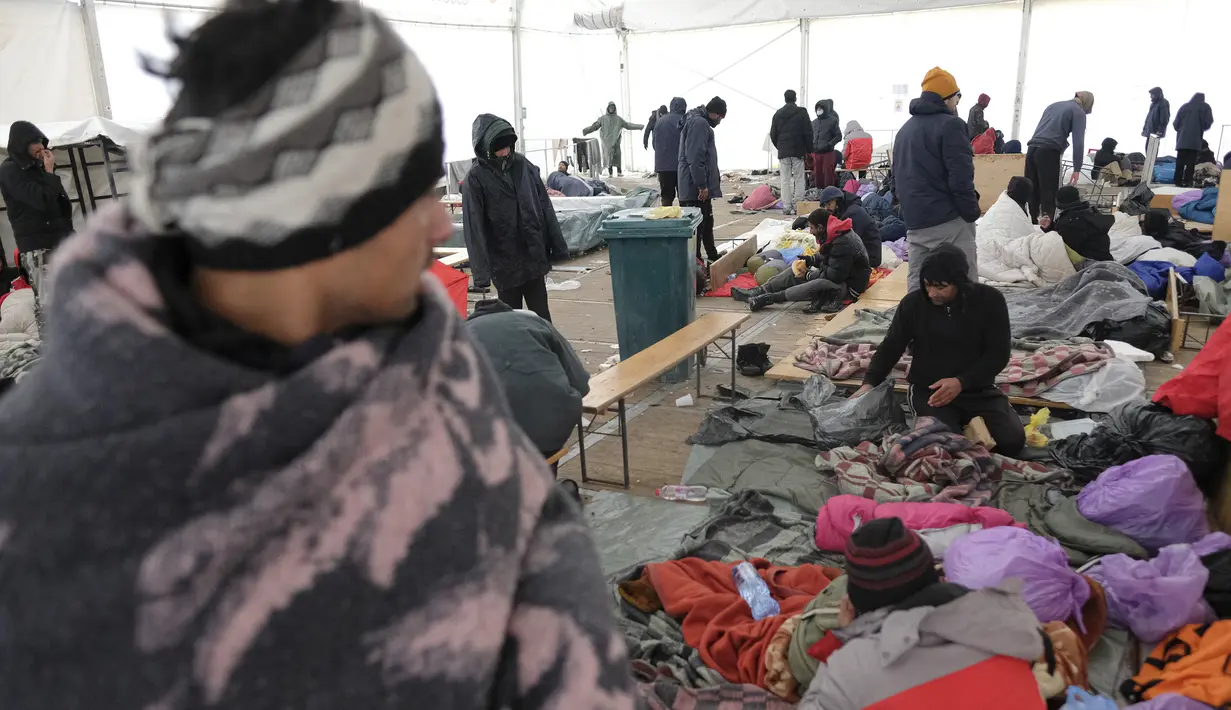 Para migran duduk di tempat penampungan sementara di kamp Lipa, barat daya Bosnia, dekat perbatasan dengan Kroasia, Sabtu (26/12/2020). Para imigran membungkus tubuh mereka dalam balutan selimut dan kantong tidur untuk melindungi diri dari serangan angin dingin yang menusuk. (AP Photo/Kemal Softic)