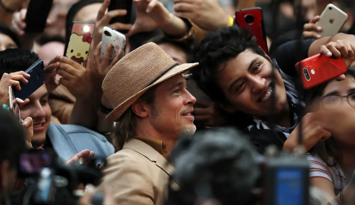 Aktor Brad Pitt berselfie dengan penggemar saat menghadiri acara karpet merah untuk film "Once Upon a Time In Hollywood" di Mexico City (12/8/2019). Aktor 55 tahun itu tampil necis dalam setelan jas krem, sepatu boot, dan kemeja mustard. (AP Photo/Marco Ugarte)
