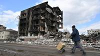 Seorang pria berjalan melewati bangunan yang hancur di kota Borodianka, barat laut Kiev pada 4 April 2022. Saat pasukan Rusia mundur, kota kecil Borodianka, 50 km barat laut Kiev, menjadi reruntuhan. (Sergei SUPINSKY / AFP)
