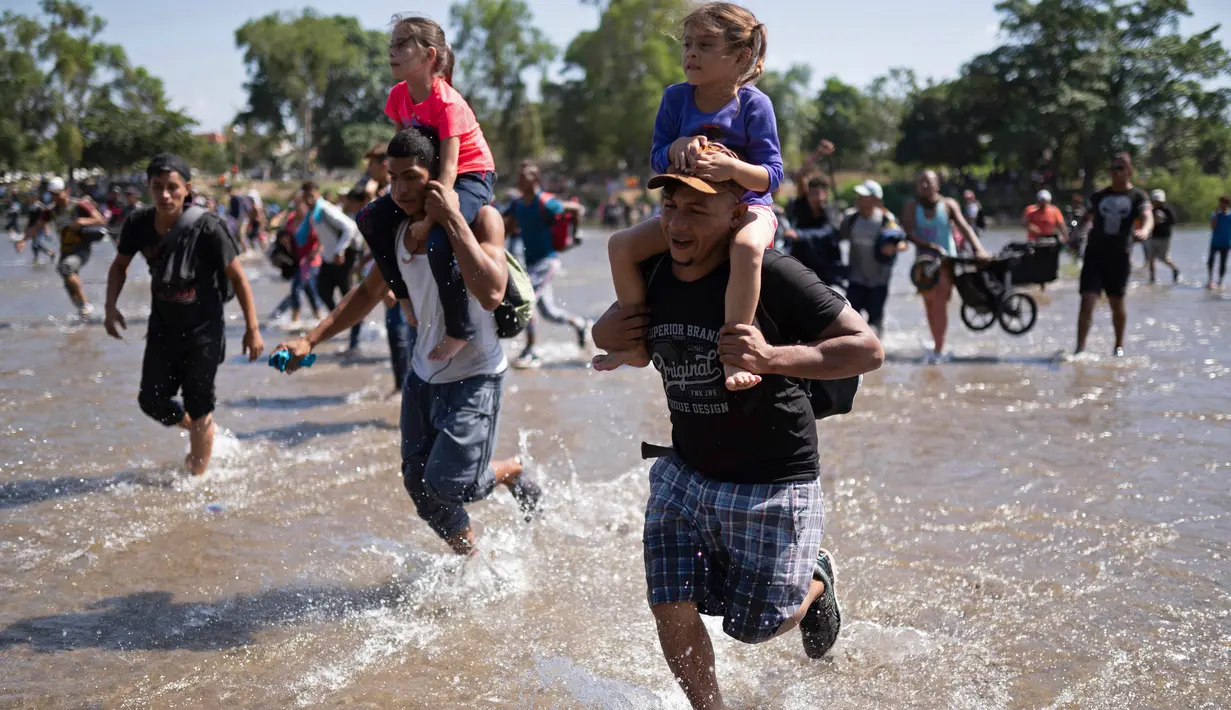 Migran Amerika Tengah membawa anak-anak saat berlari menyeberangi Sungai Suchiate dari Guatemala ke Meksiko, Ciudad Hidalgo, Meksiko, Senin (20/1/2020). Lebih dari seribu migran Amerika Tengah yang terdampar di Guatemala berjalan massal untuk menuju Amerika Serikat. (AP Photo/Santiago Billy)