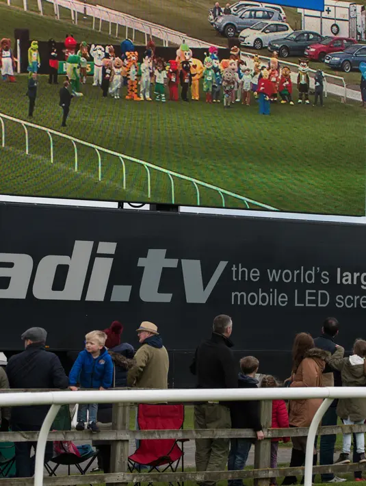 Penonton melihat layar yang menggambarkan peserta lomba lari Mascot Gold Cup bersiap memulai balapan di Wetherby Racecourse, Inggirs (29/4). (AFP/Oli Scarff)