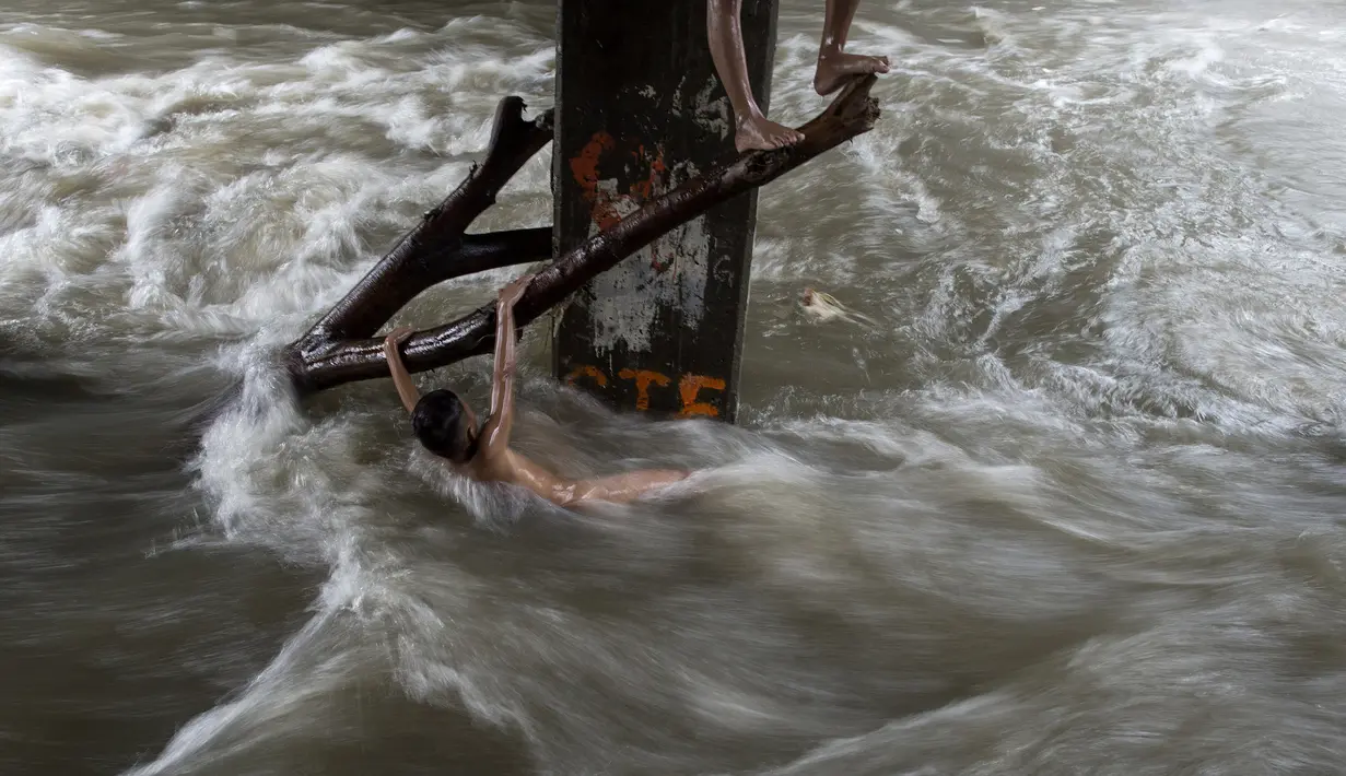 Seorang bocah laki-laki memegang batang pohon saat ia bermain di sungai dengan arus yang sangat deras akibat hujan lebat di bawah jembatan di Manila, Filipina (11/6). (AFP Photo/Noel Celis)