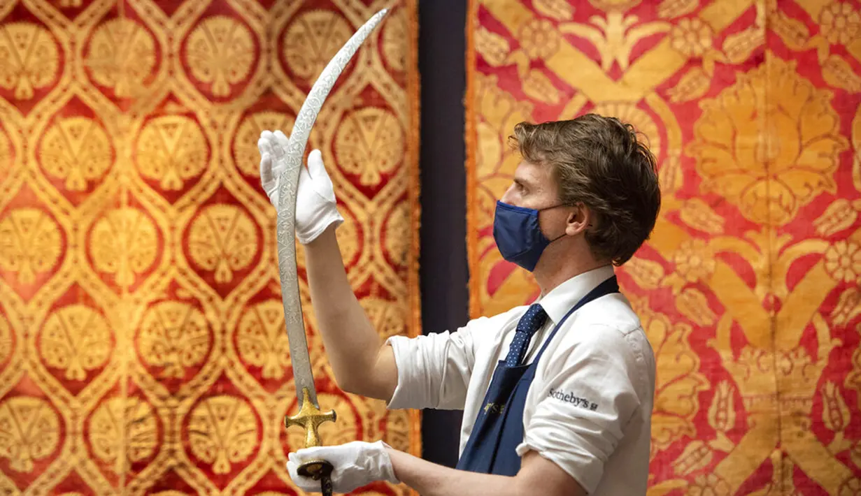 Karyawan rumah lelang Sotheby memegang pedang Talwar dengan gagang baja abad ke-19, yang menampilkan desain yang menunjukkan sepuluh avatar Dewa Wisnu, sebagai bagian dari penjualan Arts of the Islamic World dan India pada 31 Maret di London, Inggris, Senin (29/3/2021). (Dominic Lipinski/PA via AP)