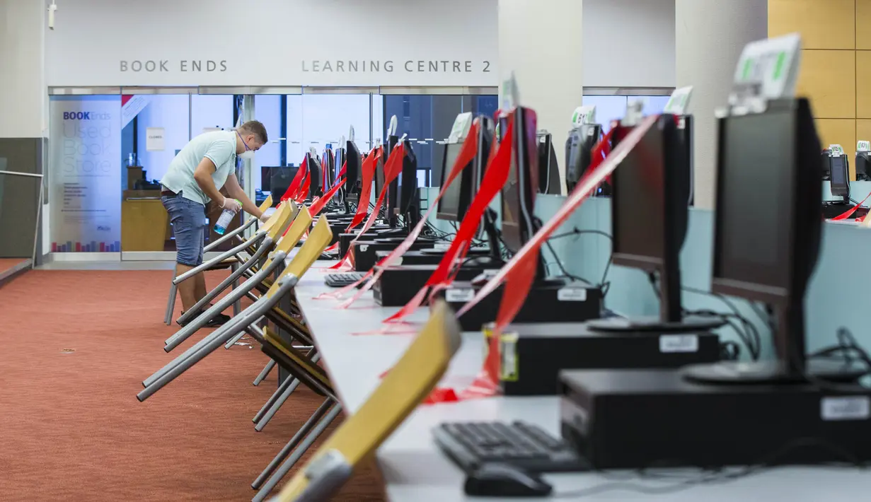 Seorang staf yang memakai masker membersihkan komputer dan meja di sebuah perpustakaan di Toronto, Kanada (24/8/2020). Tahap ketiga rencana pembukaan kembali Perpustakaan Umum Toronto dimulai pada Senin (24/8). (Xinhua/Zou Zheng)