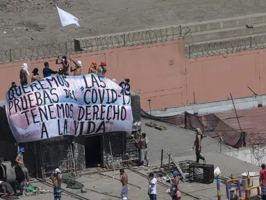 Narapidana membentangkan spanduk bertulis "Kami ingin tes COVID-19, kami memiliki hak untuk hidup” saat protes di Penjara Lurigancho, Lima, Peru, Selasa (28/4/2020). Narapidana mengeluhkan pihak berwenang tidak berbuat cukup untuk mencegah penyebaran COVID-19 dalam penjara. (AP Photo/Rodrigo Abd)