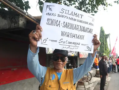 Warga menunjukkan poster bertuliskan selamat untuk pernikahan putri Presiden Jokowi,  Kahiyang Ayu dan Bobby Nasution saat menyaksikan prosesi kirab kereta kencana menuju Gedung Graha Saba di Surakarta, Rabu (8/11). (Liputan6.com/Angga Yuniar)