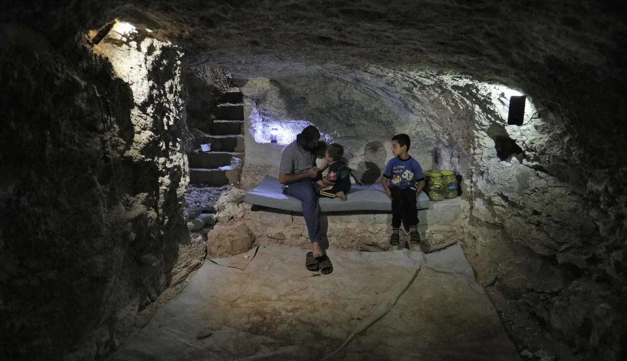 Warga Suriah, Hadheefa al-Shahadh duduk bersama anak-anaknya di dalam gua yang dia gali dalam rumahnya di Desa Maud Shurin, Provinsi Idlib, Selasa (11/). Pasukan Suriah dikabarkan akan melancarkan serangan besar-besaran ke Idlib. (OMAR HAJ KADOUR/AFP)