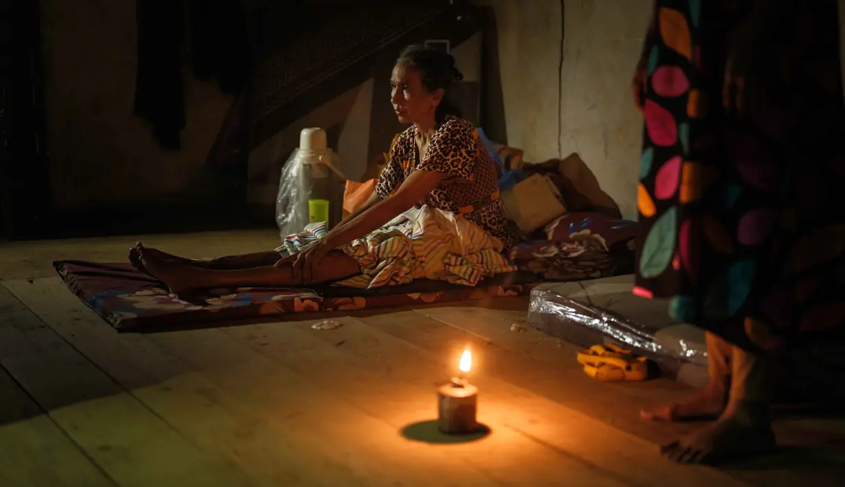 Seperti yang terlihat dalam foto berikut yang memperlihatkan suasana malam di salah satu tenda darurat pengungsi saat malam hari. Tampak dalam foto, Nurlimah, 65 tahun, yang tidak dapat berjalan sejak mengalami cedera dalam kecelakaan tabrak lari setahun lalu, duduk sambil berlindung di rumah tetangga yang sebagian runtuh di sebelah rumahnya, yang hanyut terbawa aliran banjir bandang sekitar tiga minggu sebelumnya di Aceh Tamiang, pada Selasa 16 Desember 2025. (Yasuyoshi Chiba/AFP)