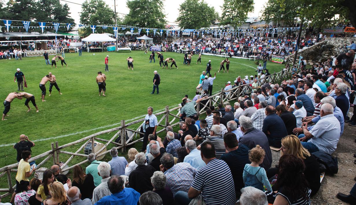 Sejumlah penonton menyaksikan kompetisi tahunan gulat minyak tradisional di Sochos, Yunani, 30 Juni 2018. Lebih dari seratus drum minyak zaitun habis untuk melumuri sekujur tubuh setiap peserta. (AP/Giannis Papanikos)