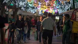 Orang-orang berjalan di bawah lampu Natal yang menghiasi jalan Santa Cruz de Tenerife di pulau Canary Tenerife, Spanyol (19/12). (AFP Photo/Desiree Martin)