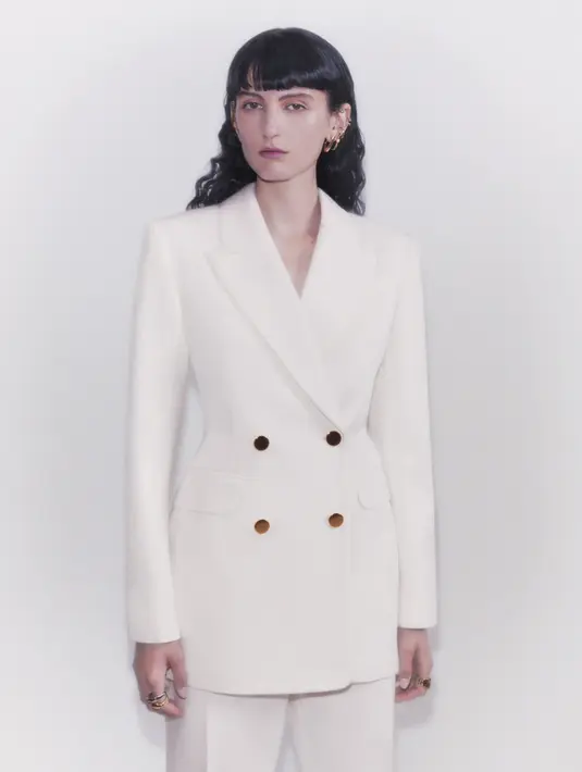 Blazer dengan warna putih gading yang sesuai dengan pantsnya. Blazer tersebut dilengkapi dengan kancing warna emas.