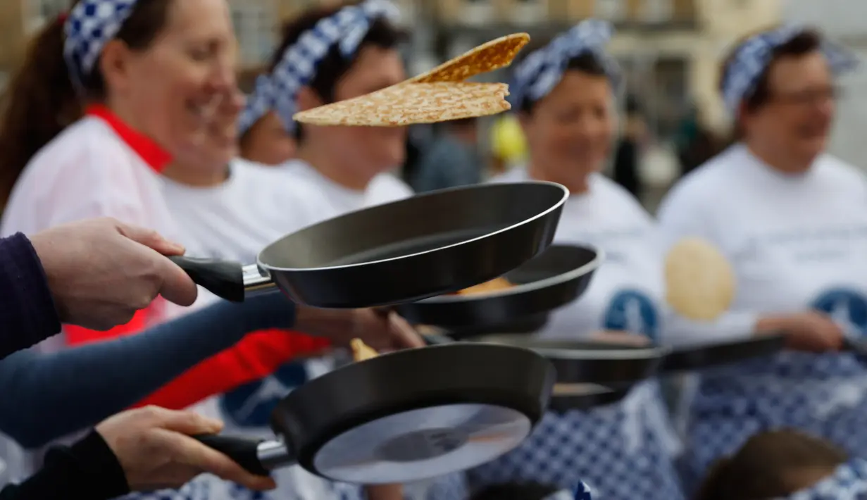 Peserta melemparkan pancake mereka sebelum mengambil bagian dalam lomba lari sembari membawa wajan di Olney, Buckinghamshire, Inggris, Selasa (25/2/2020). Para peserta kompetisi tahunan tersebut harus membolak-balikan pancake sambil tetap berlari. (AP/Alastair Grant)