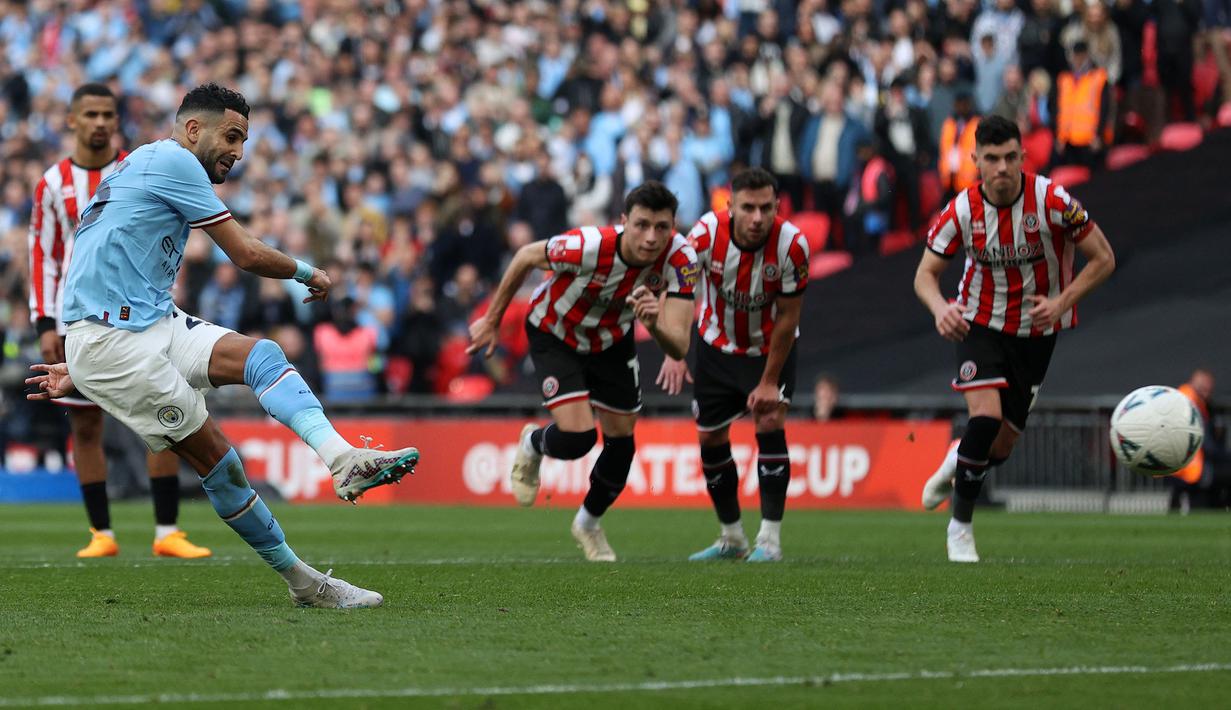 Pemain Manchester City, Riyad Mahrez (kiri) mencetak gol pembuka timnya melalui tendangan penalti pada laga semifinal Piala FA 2022/2023 melawan Sheffiled United di Stadion Wembley, London, Minggu (23/04/2023) WIB. The Cityzens sukses meraih kemenangan melalui hattrick Mahrez. (AFP/Adrian Dennis)