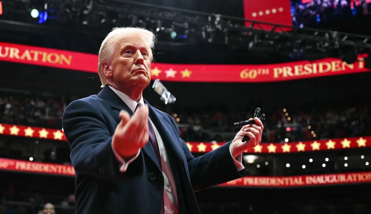 Presiden Amerika Serikat, Donald Trump melemparkan pena ke arah kerumunan setelah menandatangani perintah eksekutif selama parade perdana di dalam Capital One Arena, Washington, DC pada 20 Januari 2025. (Jim WATSON/AFP)