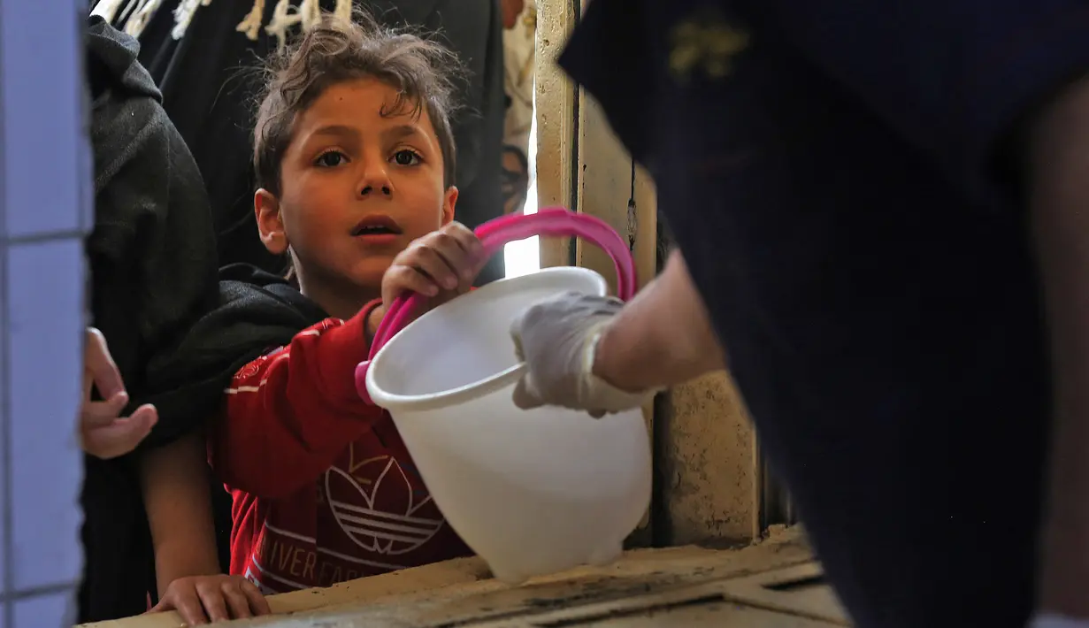 Seorang anak yang membutuhkan menerima makanan berbuka puasa dari juru masak di dapur Masjid Muslim Sunni Abdel Kader al-Kilani, Baghdad, Irak, 19 April 2021. Kegiatan ini berlangsung selama bulan suci Ramadhan. (AHMAD AL-RUBAYE/AFP)