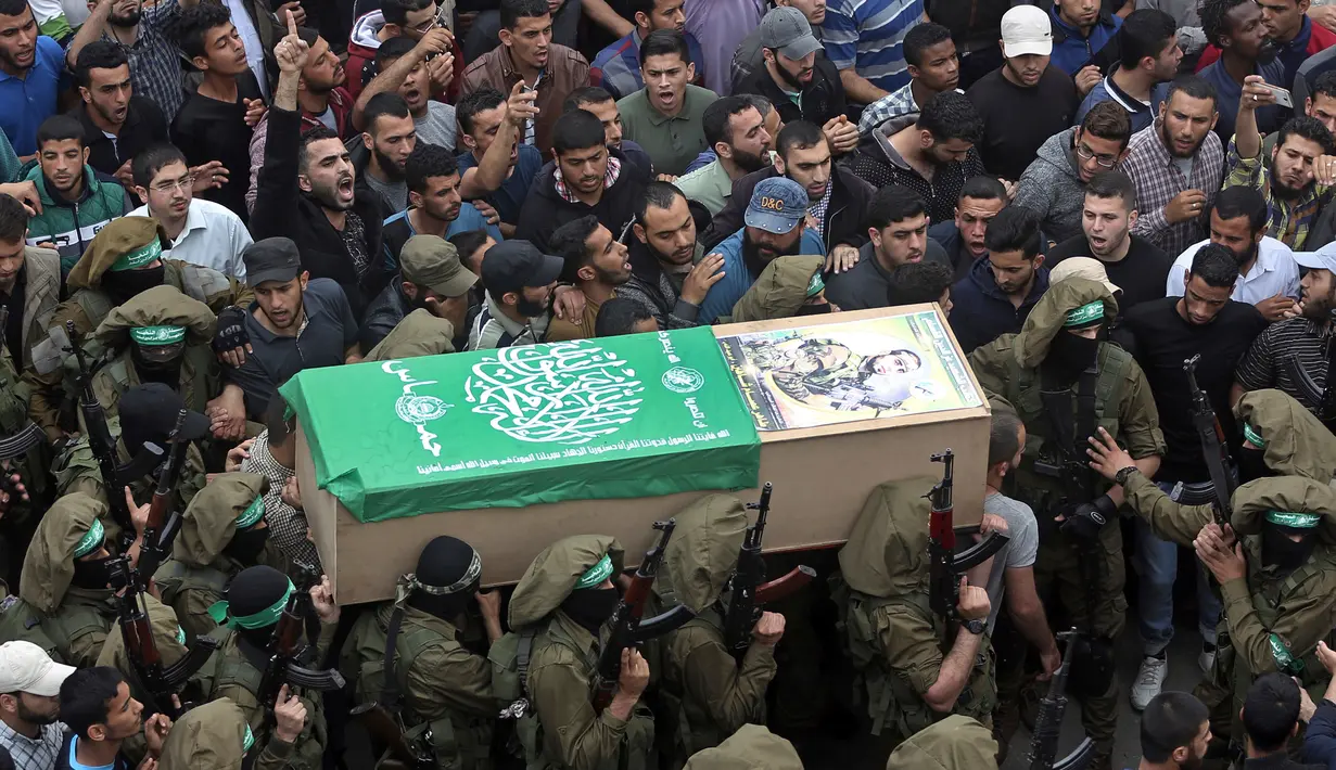 Tentara Hamas mengenakan topeng dan membawa senjata mengiringi peti jenazah enam pejuang mereka yang tewas di Deir el-Balah, Jalur Gaza (6/5). Di sisi lain, pihak militer Israel membantah terlibat dalam ledakan tersebut. (AP/Khalil Hamra)