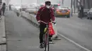Seorang pria mengenakan masker mengendarai sepedanya di jalan pada hari yang tercemar polusi udara di Beijing, China (2/4). (AFP Photo/Fred Dufour)