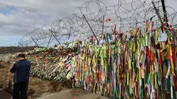 Seorang pria berjalan di dekat pagar kawat yang dihiasi ribuan pita bertuliskan pesan damai antara Korea Selatan dan Korea Utara di Paviliun Imjingak, Paju, Korea Selatan, Senin (5/3). (AP Photo/Lee Jin-man)
