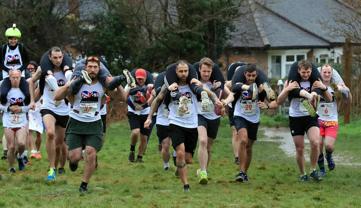 Para peserta bersaing dalam Lomba Lari Gendong Istri di The Nower, Dorking, Inggris, Minggu (3/3). Para suami harus menggendong istri mereka dari garis start hingga finish. (Gareth Fuller/PA via AP)