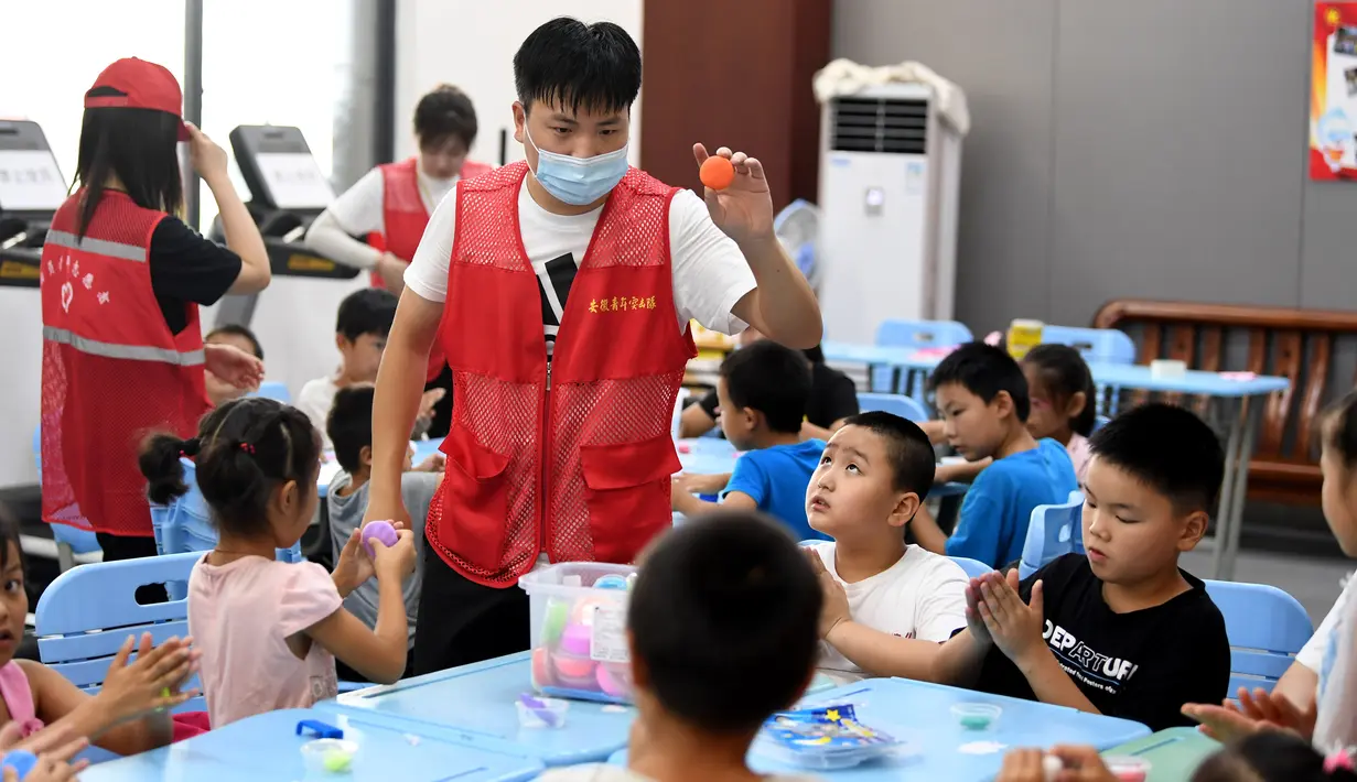 Sukarelawan bermain bersama anak-anak di tempat pengungsian sementara Sekolah Menengah No.168, Hefei, Provinsi Anhui, China, Rabu (29/7/2020). Lebih dari 300 penduduk desa di Kota Sanhe, Hefei, dievakuasi ke sekolah itu akibat terdampak banjir. (Xinhua/Liu Junxi)