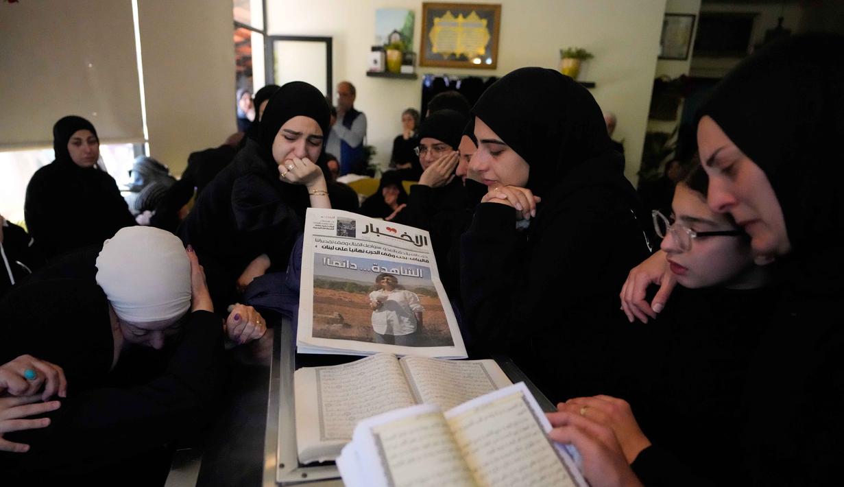 Tidak hanya Amal Khalil, serangan udara Israel di Kota al-Tayri, Lebanon Selatan, juga menewaskan sedikitnya lima orang. Tampak dalam foto, para pelayat berkumpul di sekitar peti jenazah jurnalis Lebanon Amal Khalil yang tewas dalam serangan udara Israel pada Rabu 22 April 2026, memegang koran yang menampilkan potret saudara perempuannya, menjelang prosesi pemakamannya di desa Baysariyeh, Lebanon Selatan, Kamis, 23 April 2026. (AP Photo/Mohammed Zaatari)