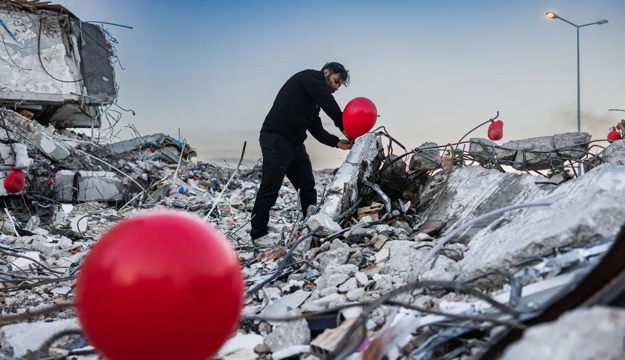 Ogun Sever Okur, pria Turki berusia 38 tahun menggantung balon di atas puing-puing bangunan yang runtuh di Antakya, Turki selatan pada 21 Februari 2023, menyusul gempa berkekuatan 6,4 yang melanda pada 20 Februari, dua minggu setelah gempa berkekuatan 7,8 gempa berkekuatan besar melanda dekat Gaziantep dan telah menewaskan lebih dari 44.000 orang. (AFP/Sameer Al-Doumy)