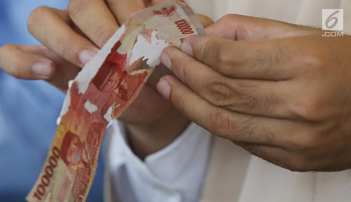 Karyawan memegang uang kertas 100 ribu rupiah di tempat penukaran uang rusak di Gedung Bank Indonessia, Jakarta (4/4). Adapun syarat penukaran uang rusak adalah minimal 2/3 bagian uang masih utuh dan masih ada nomor seri. (Merdeka.com/Arie Basuki)