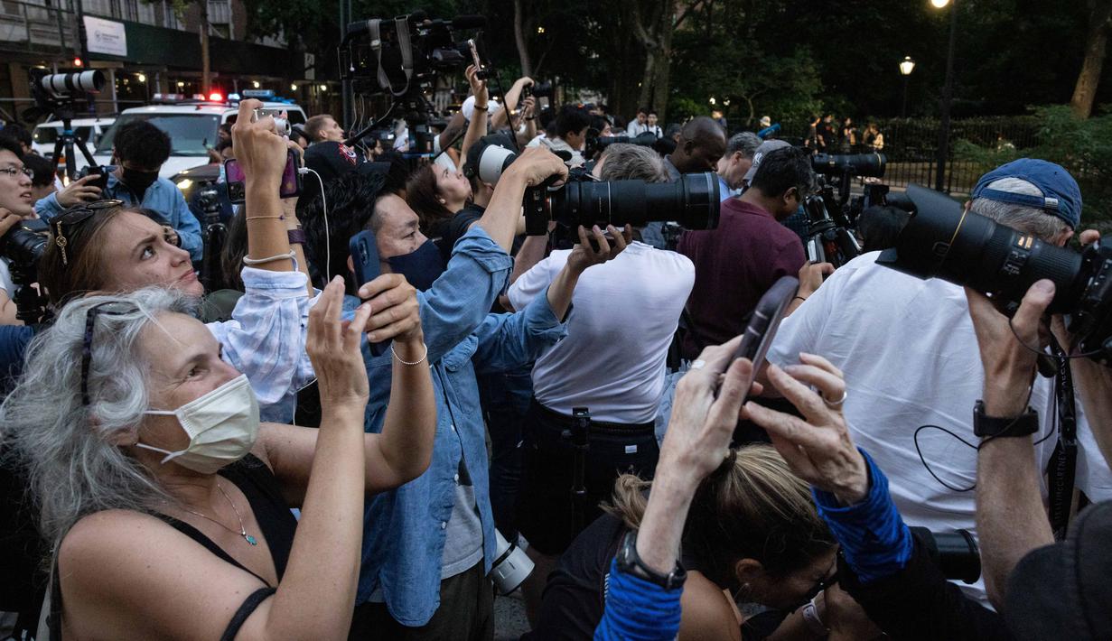 Orang-orang mengambil gambar saat matahari terbenam di Manhattan ketika fenomena "Manhattanhenge" di 42nd street, New York, Senin (11/7/2022). Dikenal dengan sebutan Manhattanhenge, fenomena terbenamnya matahari yang satu ini selalu membuat jalanan Manhattan macet. (Yuki IWAMURA / AFP)