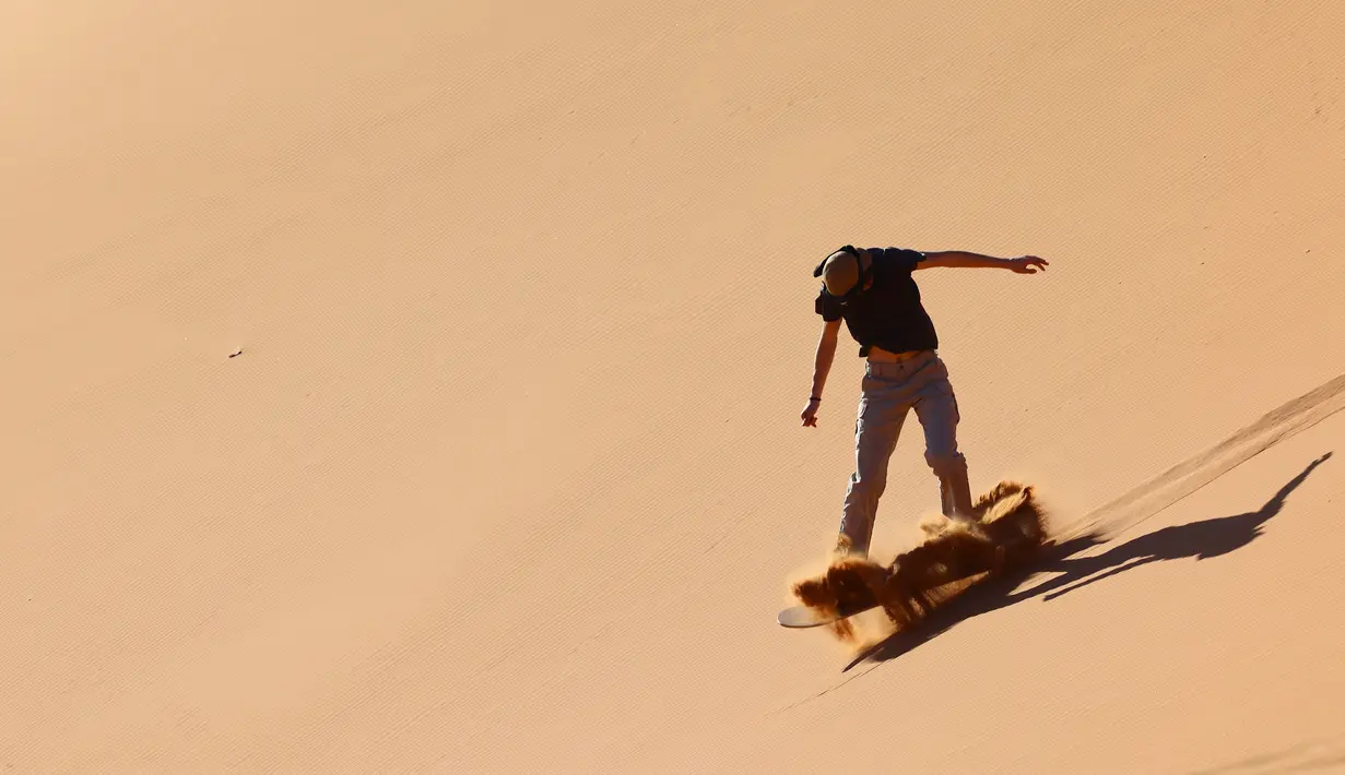 Seorang turis mencoba atraksi berseluncur dengan sandboarding di gurun Dubai pada 11 Januari 2021. Di sini para wisatawan dapat mencoba sensasi bermain sandboarding sambil memandang hamparan lautan pasir cokelat. (Photo by GIUSEPPE CACACE / AFP)