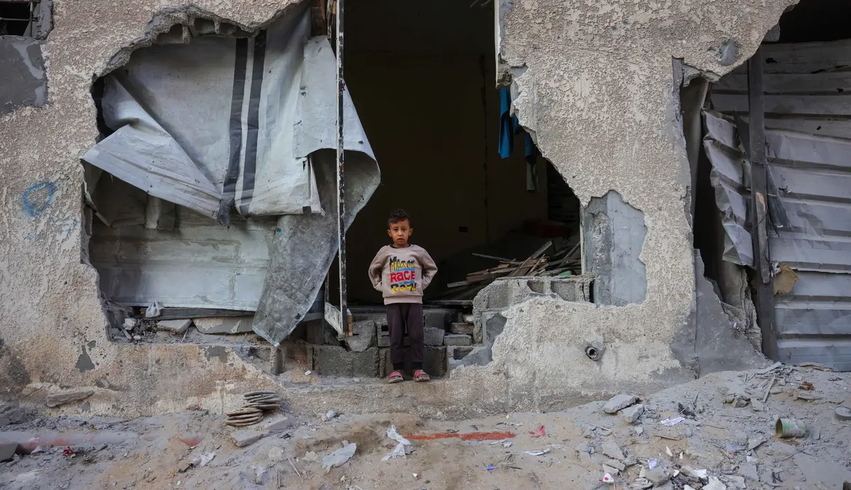 Seorang anak laki-laki berdiri di celah tembok rumahnya yang hancur akibat serangan Israel di Khan Younis, Jalur Gaza selatan, pada Rabu 29 Oktober 2025. Serangan Israel terjadi beberapa jam setelah Presiden Amerika Serikat (AS) Donald Trump mengatakan "tidak ada" yang akan membahayakan perjanjian gencatan senjata yang ia bantu mediasi. (BASHAR TALEB/AFP)