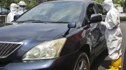 Petugas berpakaian APD lengkap melayani pasien yang secara mandiri melakukan swab test drive thru di halaman parkir rumah sakit di Jakarta, Rabu (12/5/2020). Swab test drive thru dilakukan untuk mendeteksi dan mencegah penyebaran virus corona COVID-19. (Liputan6.com/Johan Tallo)
