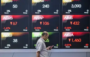 Seorang pria melihat ponselnya di depan layar yang menampilkan Indeks Harga Saham Gabungan (IHSG), yang anjlok signifikan selama pembukaan pasar, di gedung Bursa Efek Indonesia di Jakarta pada Rabu 13 Mei 2026. (BAY ISMOYO/AFP)