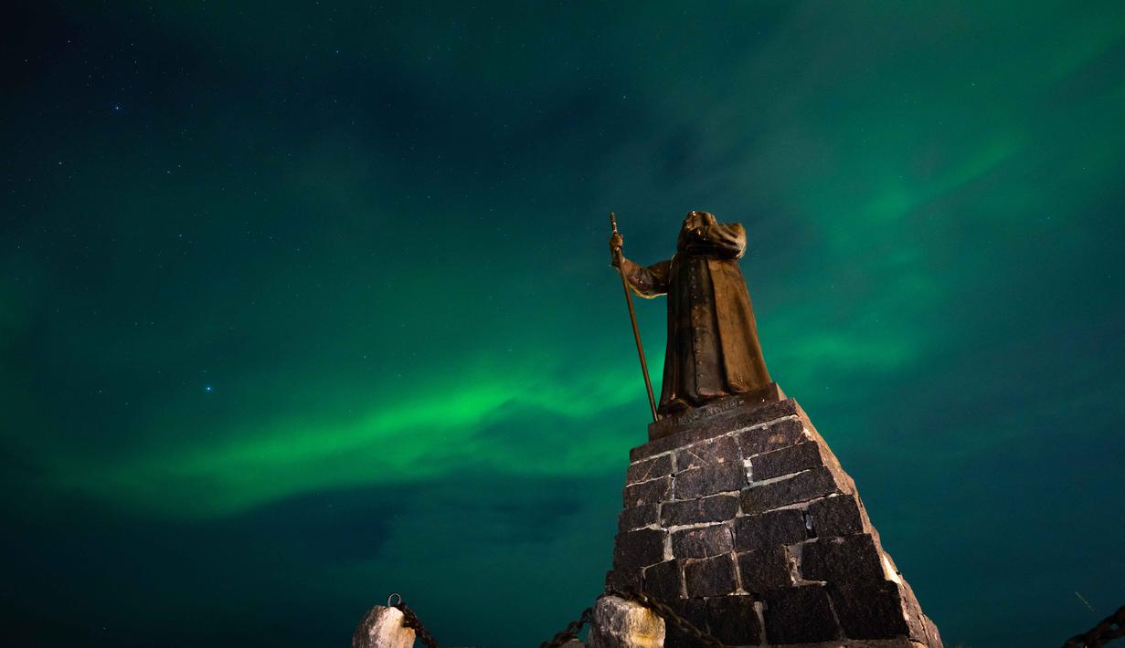 Fenomena yang menciptakan pemandangan alam yang memukau ini adalah Aurora Borealis atau cahaya utara. Tampak dalam foto, Aurora Borealis menerangi langit malam di atas patung Hans Egede yang menghadap Nuuk, Greenland, pada 23 Januari 2026. (Jonathan NACKSTRAND/AFP)