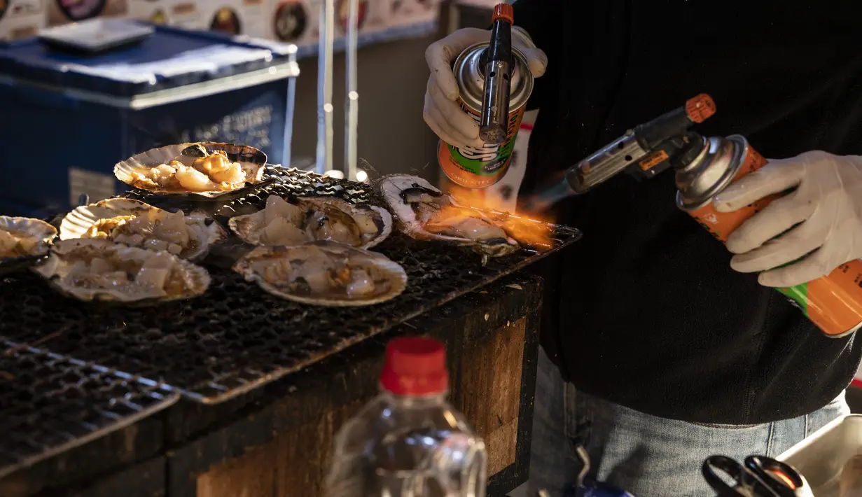 Seorang penjual menggunakan obor untuk makanan laut segar di area "pasar ikan luar" Tsukiji di Tokyo pada 28 Desember 2022. Menjelang liburan Tahun Bar, turis asing dan penduduk lokal berkunjung  ke pasar itu untuk menikmati hidangan bermacam makanan laut. (AFP/Richard A. Brooks)