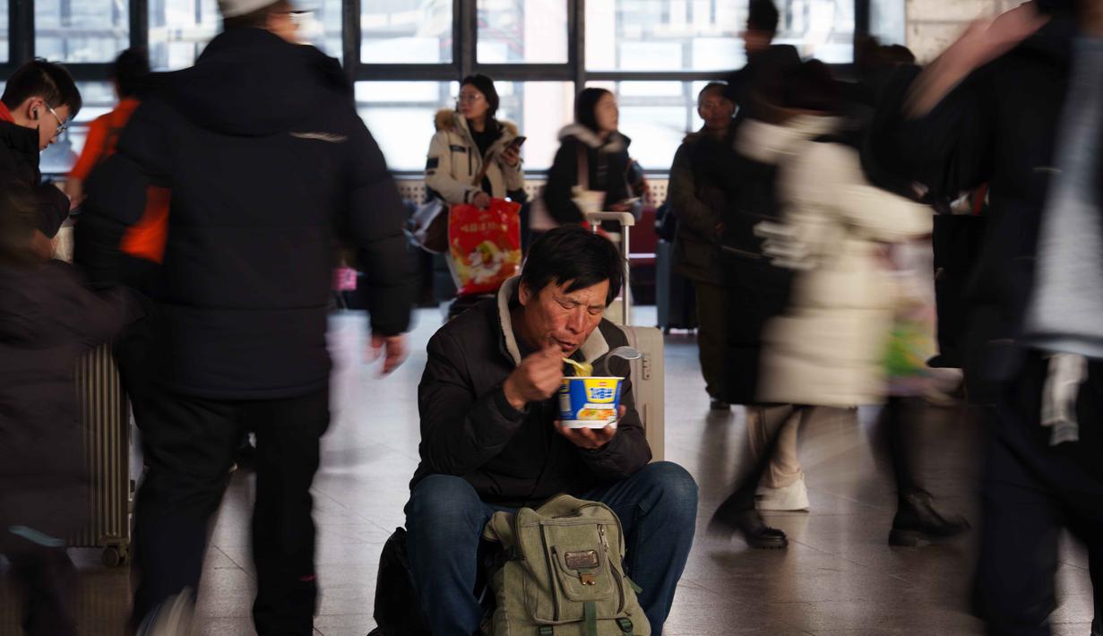 Dari total tersebut, perjalanan melalui jalan raya tetap menjadi yang dominan, mencakup sekitar 80 persen. Tampak dalam foto, seorang pelancong menikmati makanan sambil menunggu di dalam stasiun kereta api saat orang-orang pulang kampung selama liburan Tahun Baru Imlek di Beijing, China, Selasa 10 Februari 2026. (AP Photo/Vincent Thian)