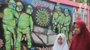 Pejalan kaki melintasi mural covid-19 di Tanah Tinggi, Tangerang, Sabtu (29/1/2022). Kasus Covid-19 varian Omicron di Indonesia terus bertambah dan wilayah penyebarannya semakin meluas. Diperkirakan, kasus omicron sudah mendominasi penularan virus corona di Jawa Bali. (Liputan6.com/Angga Yuniar)