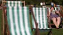 Seorang wanita membaca buku sambil menikmati sinar matahari di atas kursi di sebuah taman di London, Inggris, Rabu (4/5). Awal Mei, suhu udara hangat mulai menyelimuti kota London. (REUTERS/Neil Hall)