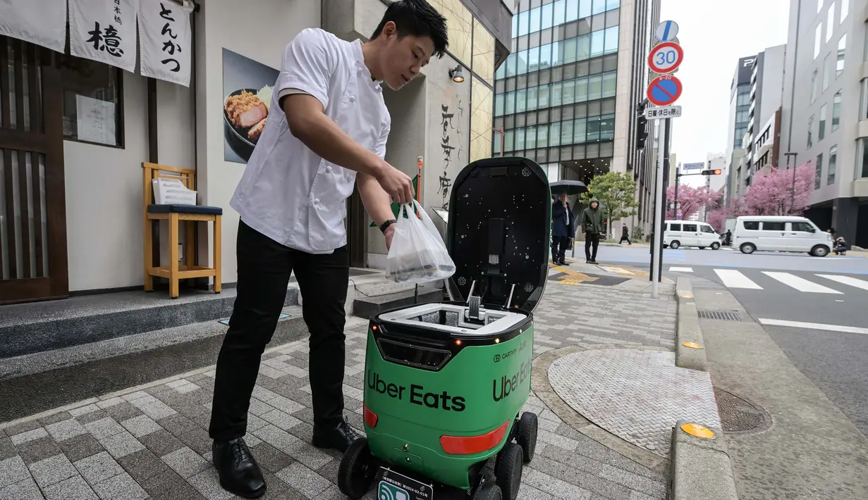<p>Seorang karyawan restoran menempatkan pesanan makanan di dalam robot tanpa awak selama uji coba layanan pengiriman robot oleh Uber Eats Japan, Mitsubishi Electric dan pengembang robot Cartken di pusat kota Tokyo pada tanggal 5 Maret 2024. (Richard A. Brooks/AFP)</p>