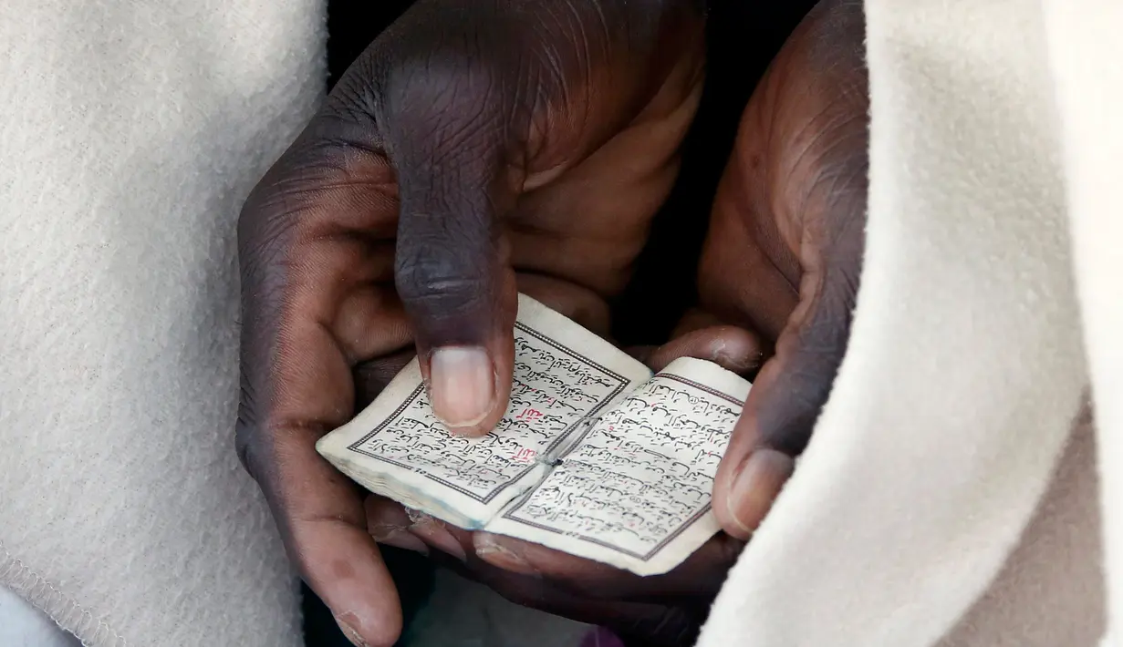 Seorang imigran dibaluti selimut saat membaca Al-Quran berukuran kecil di Saint Ludovic perbatasan Italia-Prancis, (18/6/2015). Sekitar 200 imigran berada di bebatuan pantai untuk melintasi perbatasan Italia. (REUTERS/Eric Gaillard)