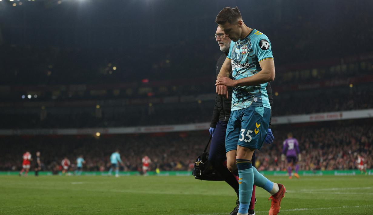 Bek Southampton, Jan Bednarek berjalan meninggalkan lapangan didampingi anggota tim medis Southampton, dr Steve Baynes saat menghadapi Arsenal pada laga Liga Inggris 2022/2023 di Emirates Stadium, London (21/4/2023). (AFP/Adrian Dennis)